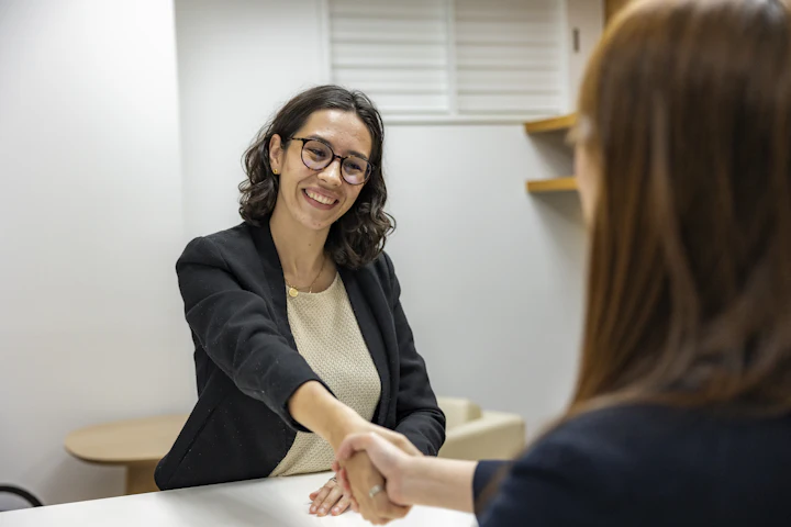 A smiling manager shaking hands with a candidate across a desk