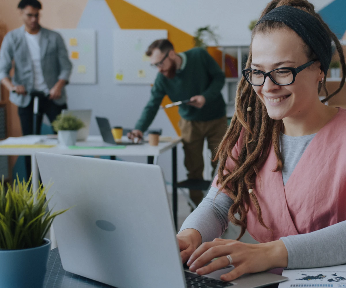 A smiling woman working on a laptop in a bright office